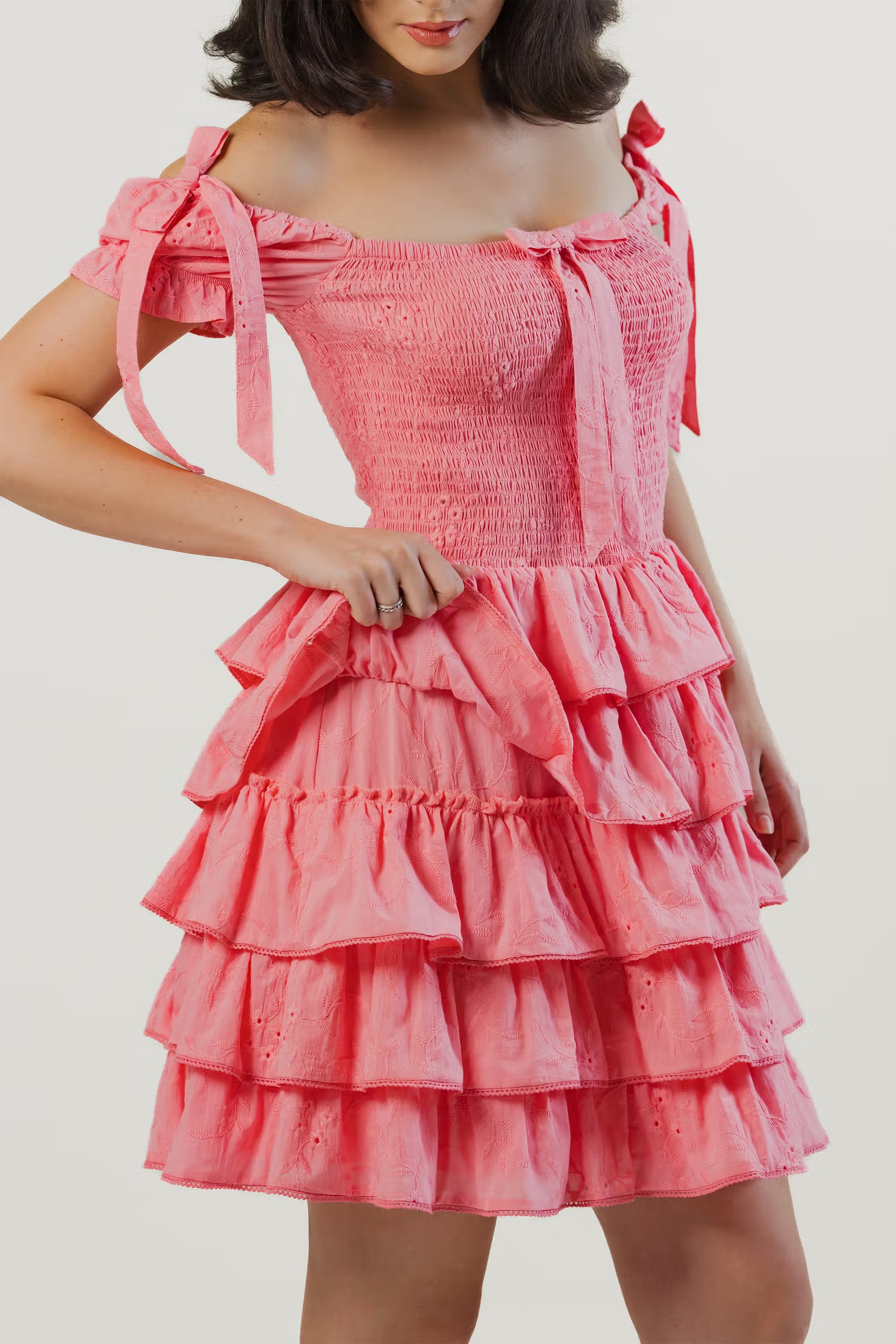 Close-up of pink ruffled mini dress showing smocked bodice, bow tie straps, and layered skirt