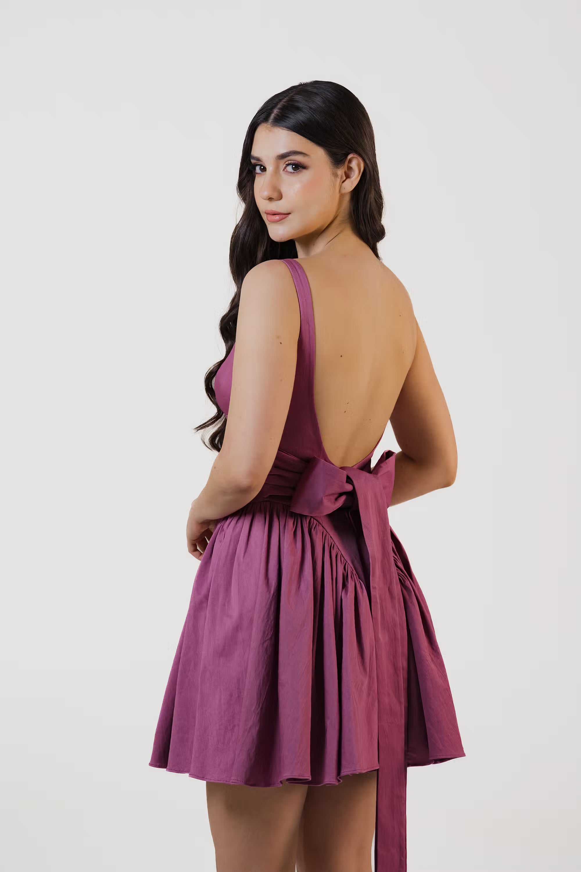 Back view of plum purple square-neck dress featuring open back with large bow tie