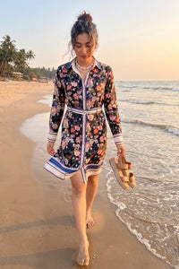 Woman walking barefoot on the beach at sunset wearing Pretty Pixie's black floral belted shirt dress with long sleeves