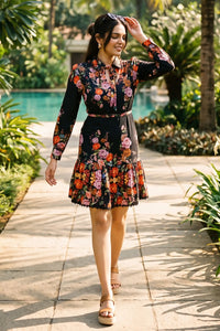 Woman in black floral high-neck belted long-sleeve mini dress with tiered ruffle hem walking poolside garden path - Pretty Pixie daywear