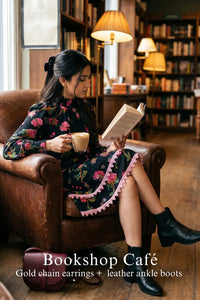 Woman in Pretty Pixie noir floral high-neck puff-sleeve mini dress styled for a bookshop cafe