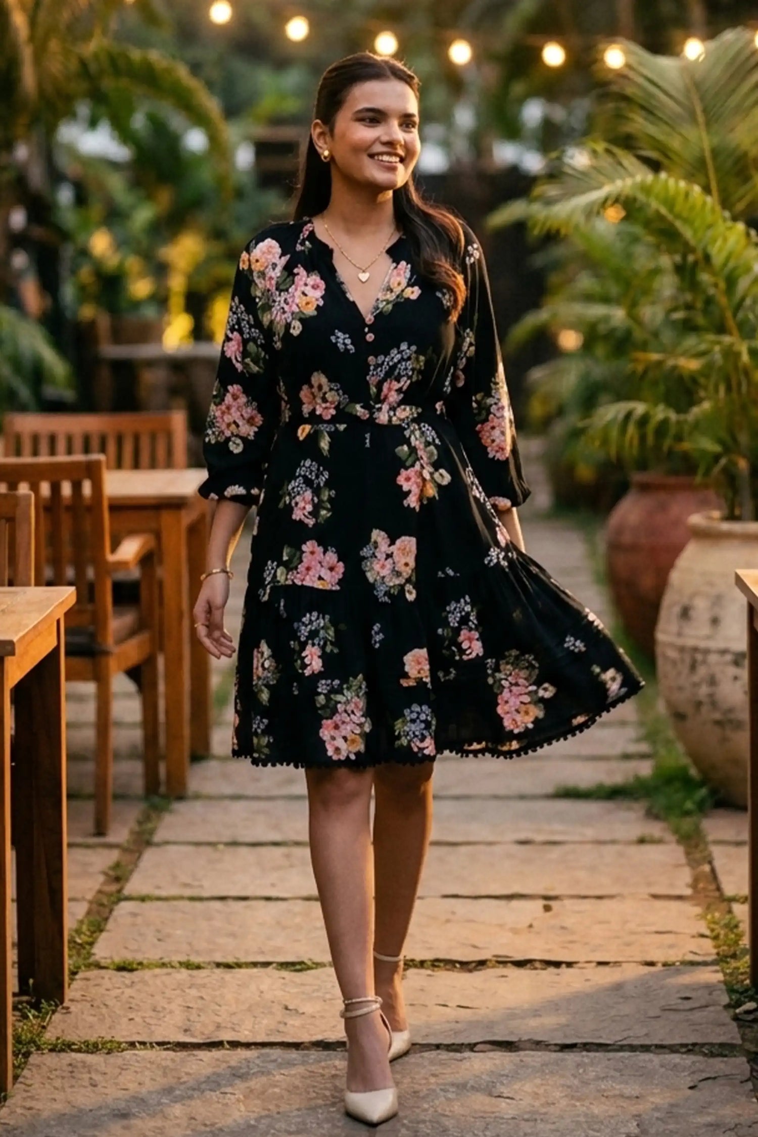Woman walking in black floral long-sleeve tiered button-down dress on lantern-lit garden path at dusk - Pretty Pixie evening wear