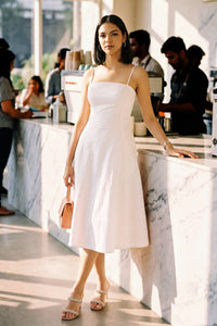 Woman standing at a marble café counter wearing Pretty Pixie's blush pink cotton spaghetti strap bustier midi dress