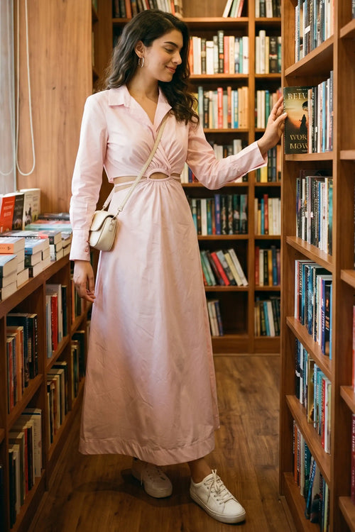 Woman browsing shelves in a bookstore wearing Pretty Pixie's blush pink cutout maxi shirt dress