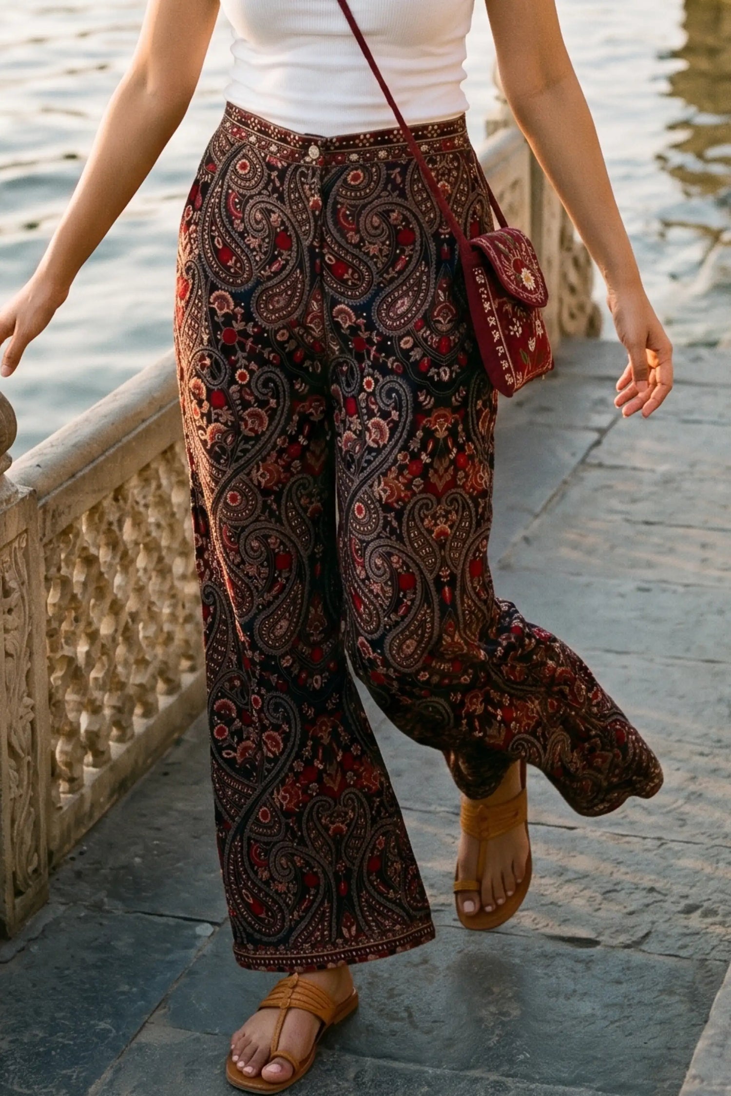 Woman in crimson paisley navy hand embroidered wide-leg pants with burgundy embroidered crossbody bag walking lakeside palace promenade - Pretty Pixie travel wear
