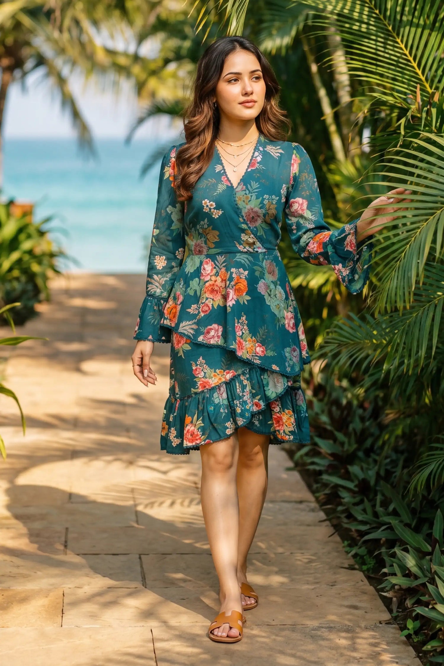 Woman in emerald floral wrap belted ruffle-hem mini dress with bell sleeves walking tropical garden path near ocean - Pretty Pixie resort wear