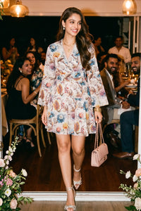 Woman smiling at a dinner party wearing Pretty Pixie's ivory floral wrap long-sleeve mini dress