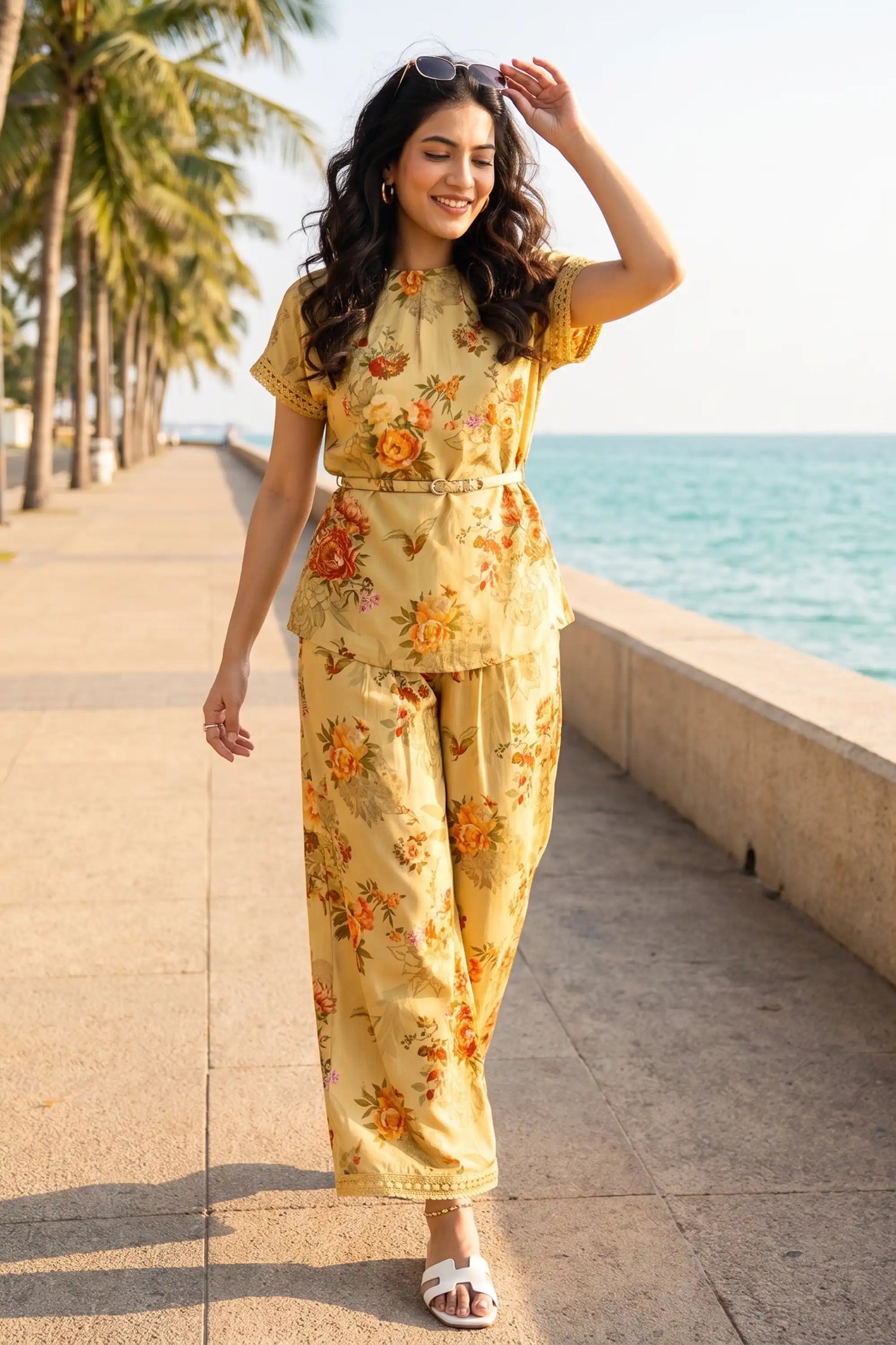 Woman in mustard yellow floral print belted co-ord set walking palm-lined seaside promenade - Pretty Pixie vacation co-ord