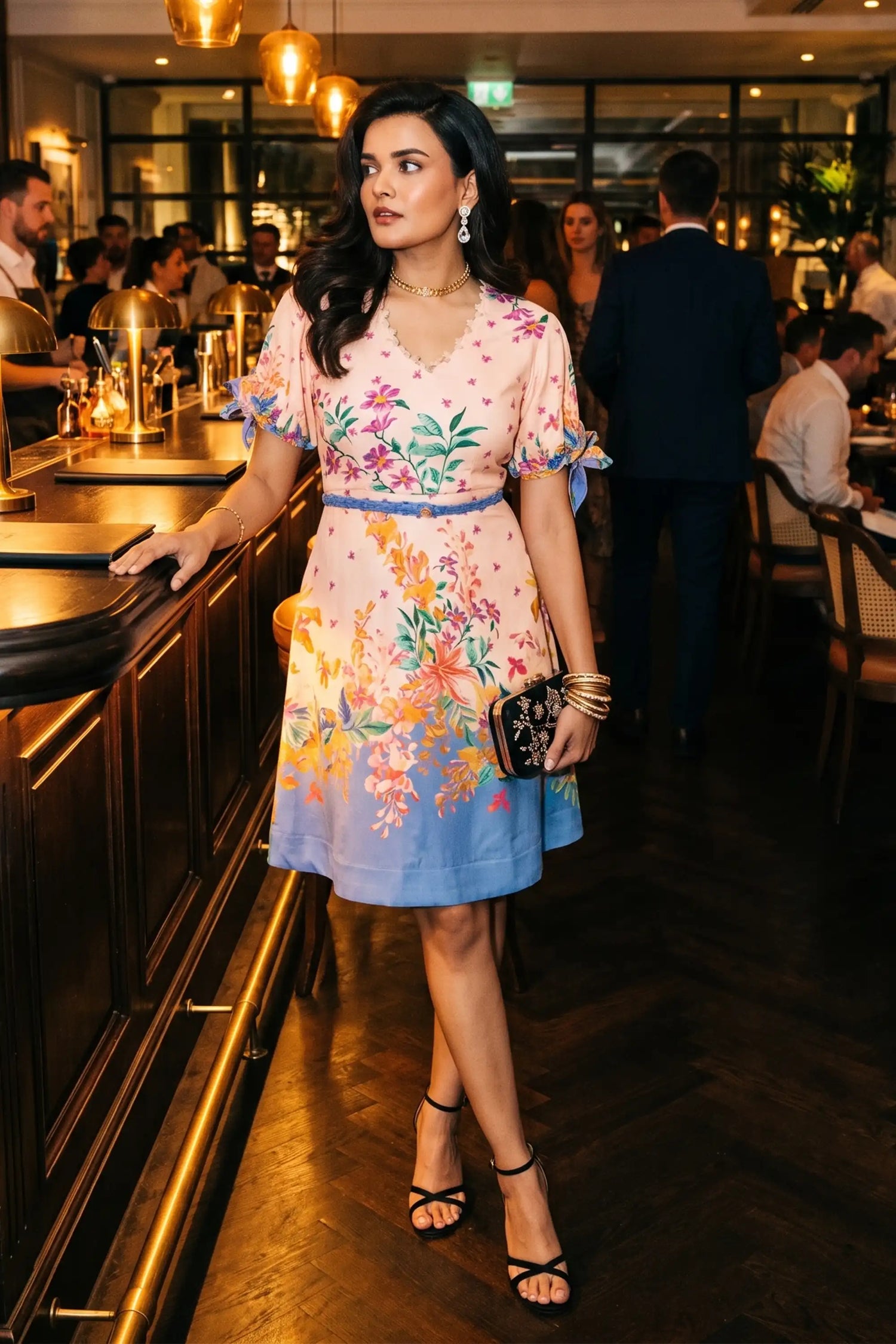 Woman in pastel pink Riviera floral V-neck mini dress with ombre hem and tie sleeves at restaurant bar in evening - Pretty Pixie evening wear