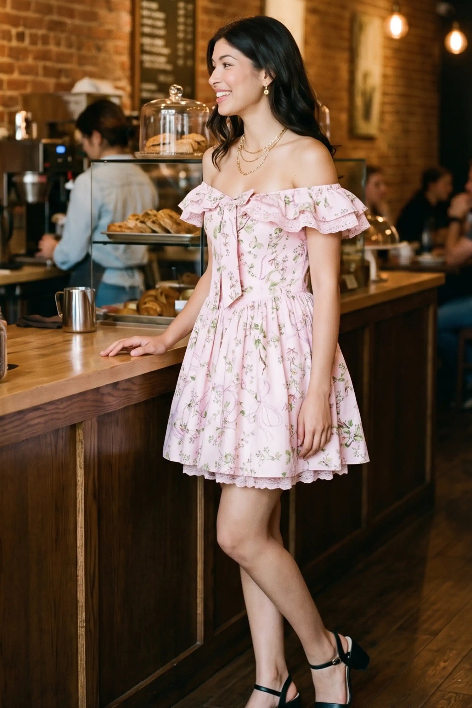 Woman smiling at a coffee shop counter wearing Pretty Pixie's pink floral lace-trim off-shoulder mini dress