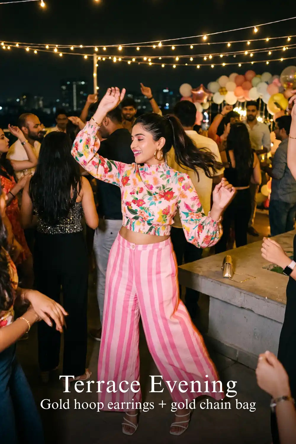 Woman in Pretty Pixie pink floral crop top & striped pants co-ord set styled for a terrace evening