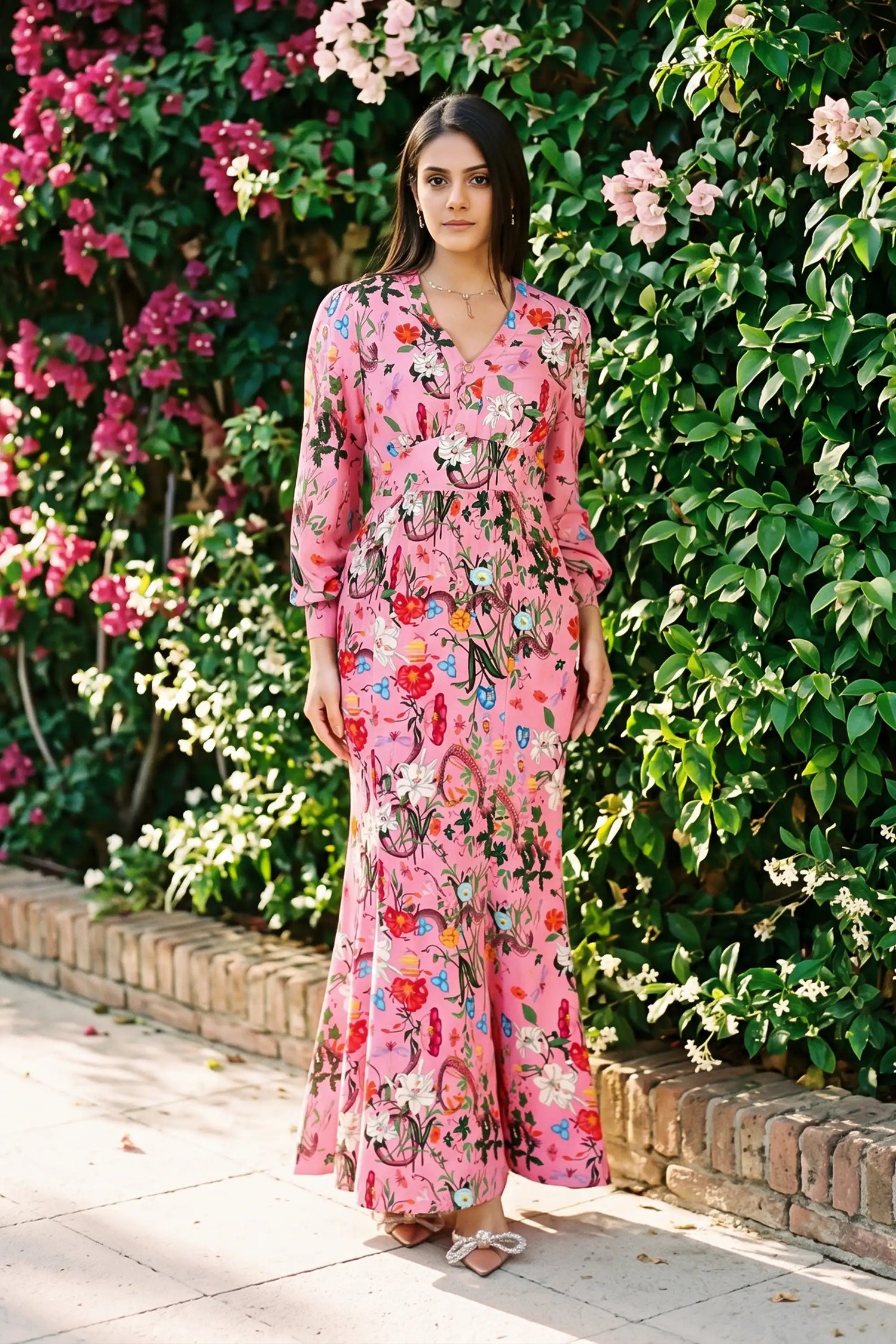 Woman in pink floral V-neck long-sleeve maxi dress with botanical lily print standing against bougainvillea garden wall - Pretty Pixie evening wear