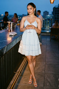 Woman holding a cocktail at a rooftop bar at dusk wearing Pretty Pixie's powder blue lace-trim spaghetti strap mini dress