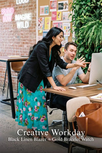 Woman in turquoise floral dress layered with black linen blazer and gold bracelet watch, pointing at computer screen in creative office
