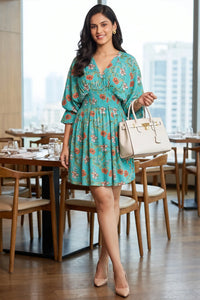 Woman smiling at a restaurant table wearing Pretty Pixie's turquoise floral puff-sleeve belted mini dress with smocked waist