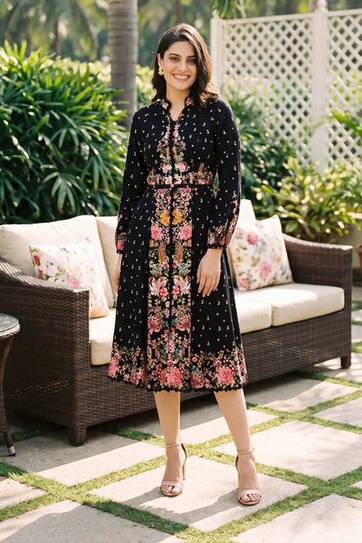 Woman in Twilight Garden black ditsy floral border midi dress with dotted print and mandarin collar smiling on patio lounge with rattan sofa - Pretty Pixie daywear