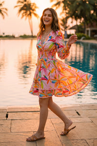 Woman twirling in vibrant floral ruffled V-neck mini dress with tropical parrot print at poolside during sunset - Pretty Pixie resort wear