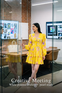 Woman in Pretty Pixie marigold tie-neck ruffle mini dress styled for a creative meeting