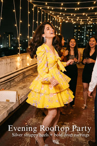 Woman in Pretty Pixie marigold tie-neck ruffle mini dress styled for an evening rooftop party 2