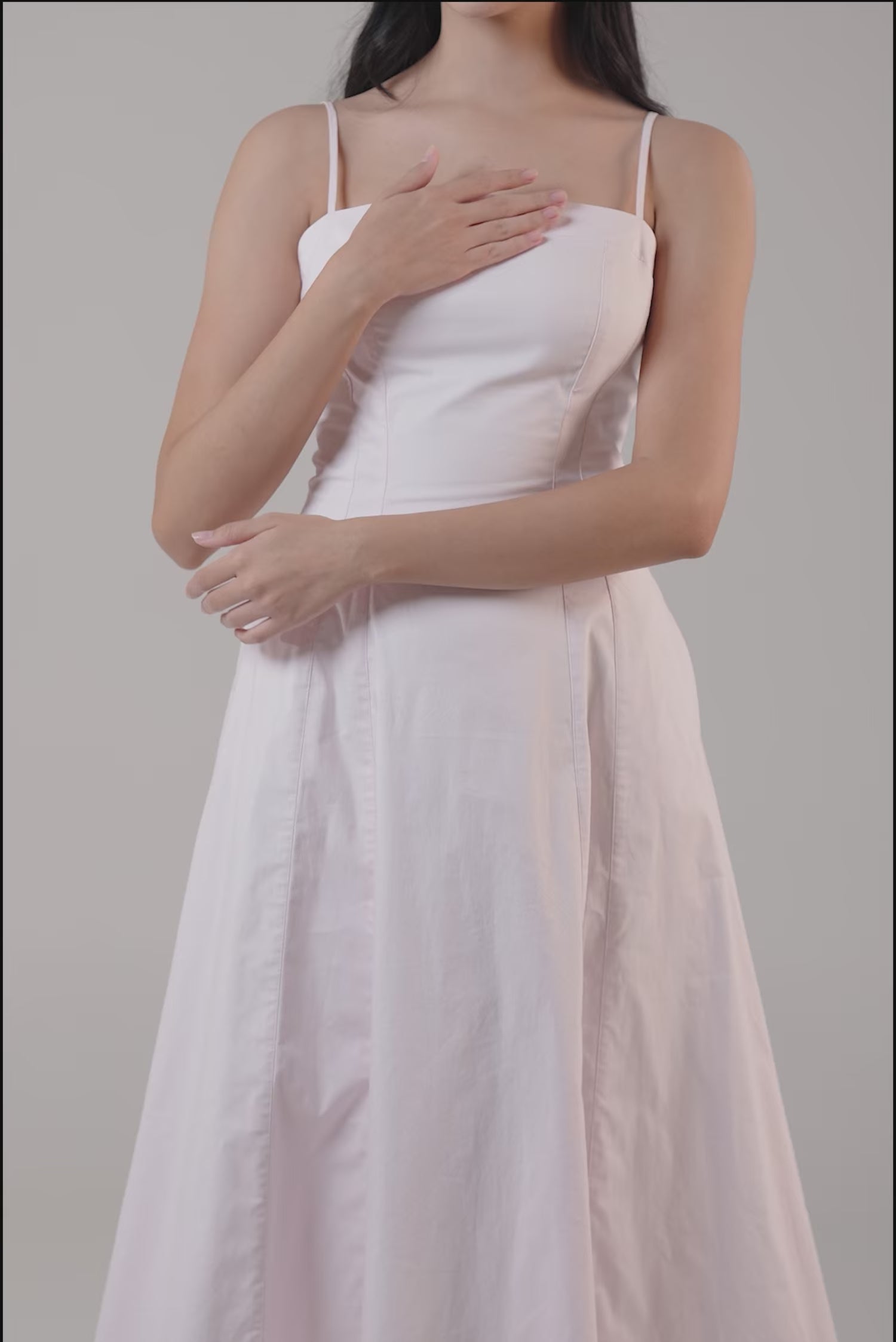 Woman wearing a pastel pink midi dress with square neckline and thin straps, styled with nude heels.