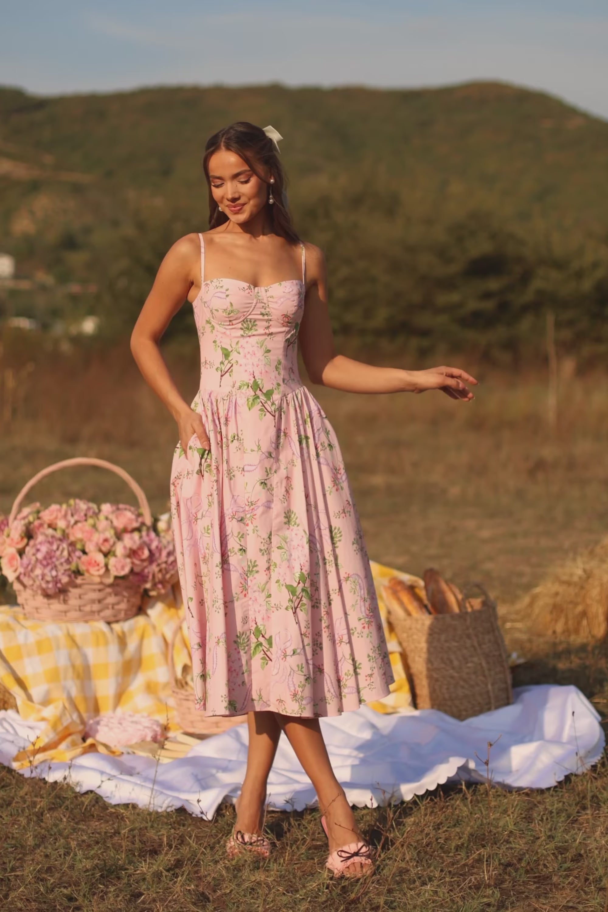 Woman wearing a pink floral midi dress by Pretty Pixie, featuring a fitted bodice and flowy skirt in a studio product video showcase.