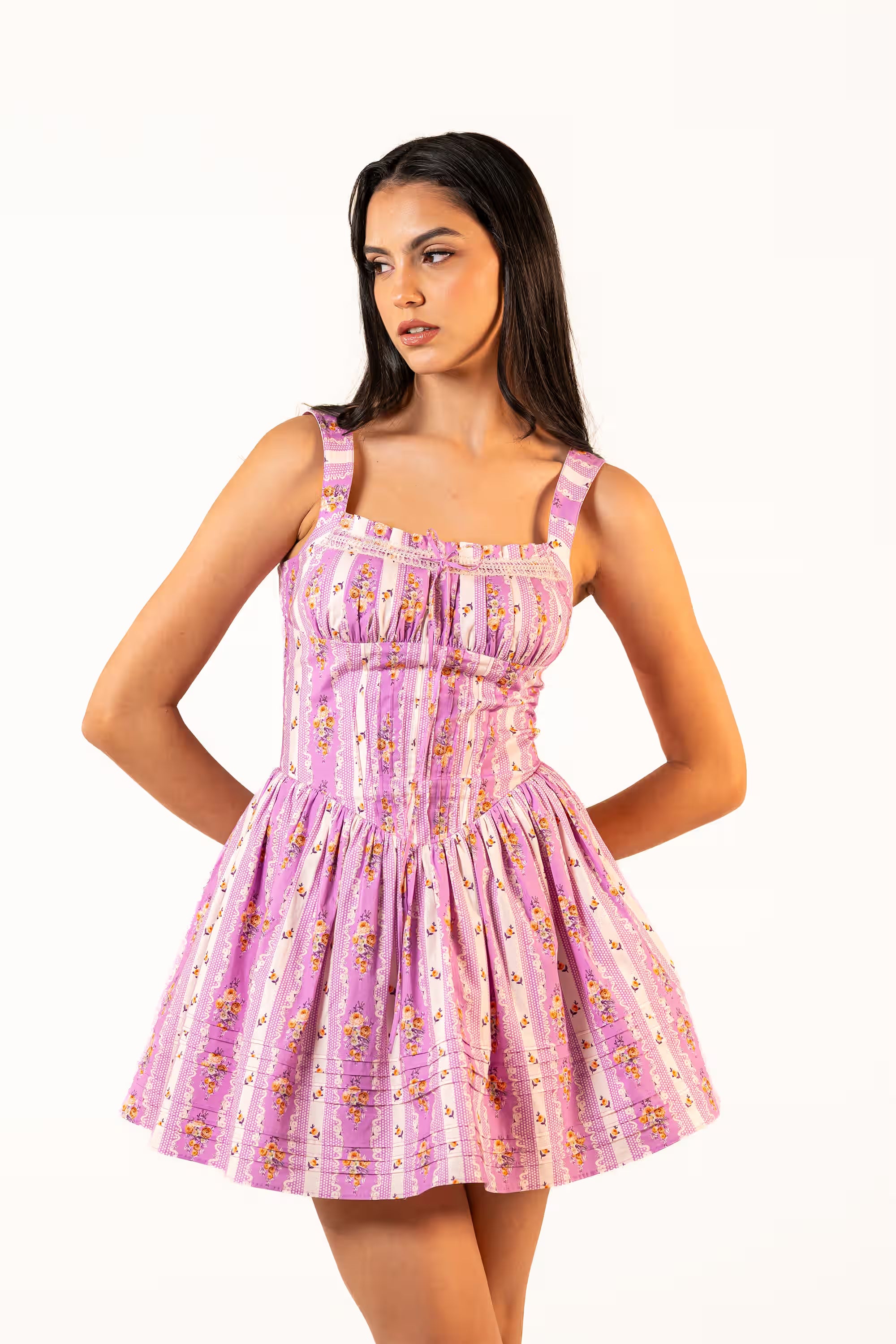 Side angled view of a purple floral mini dress with wide straps and pleated skirt.