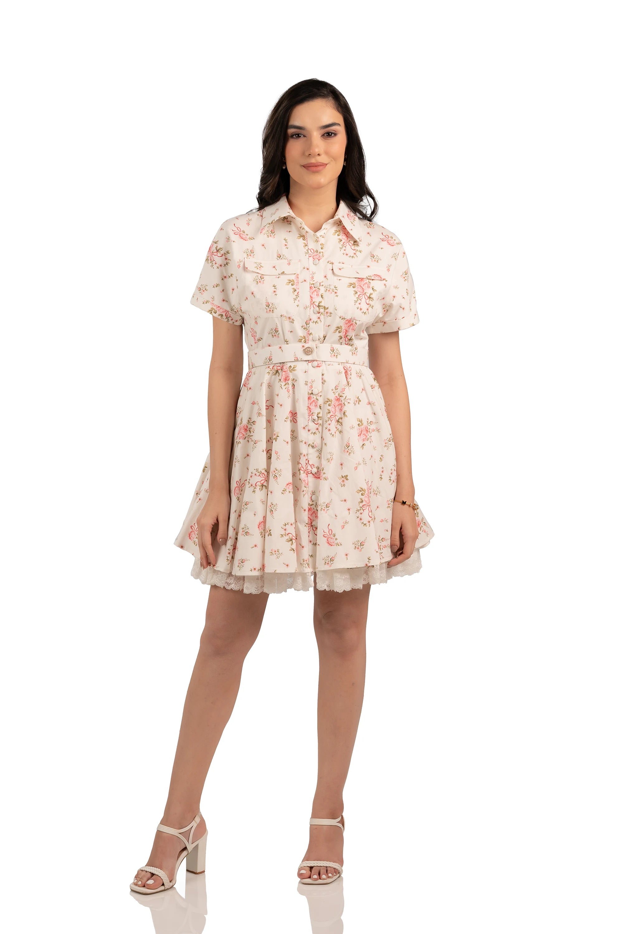 Model wearing short white floral dress with pink roses, lace hem, collared neckline, and belted waist, front view.