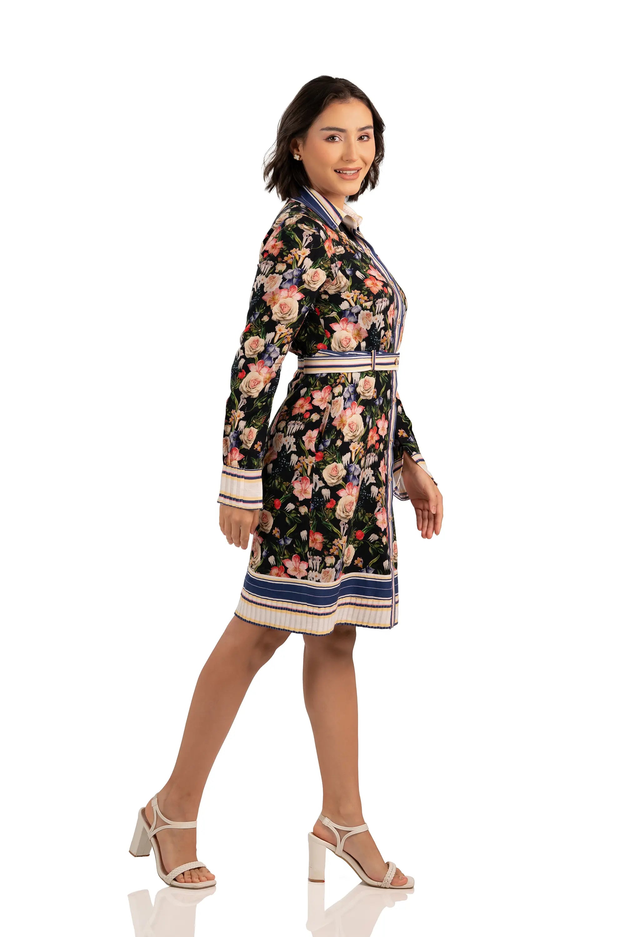 Model in side profile wearing black floral shirt dress with belted waist, long sleeves, and striped cuff details.