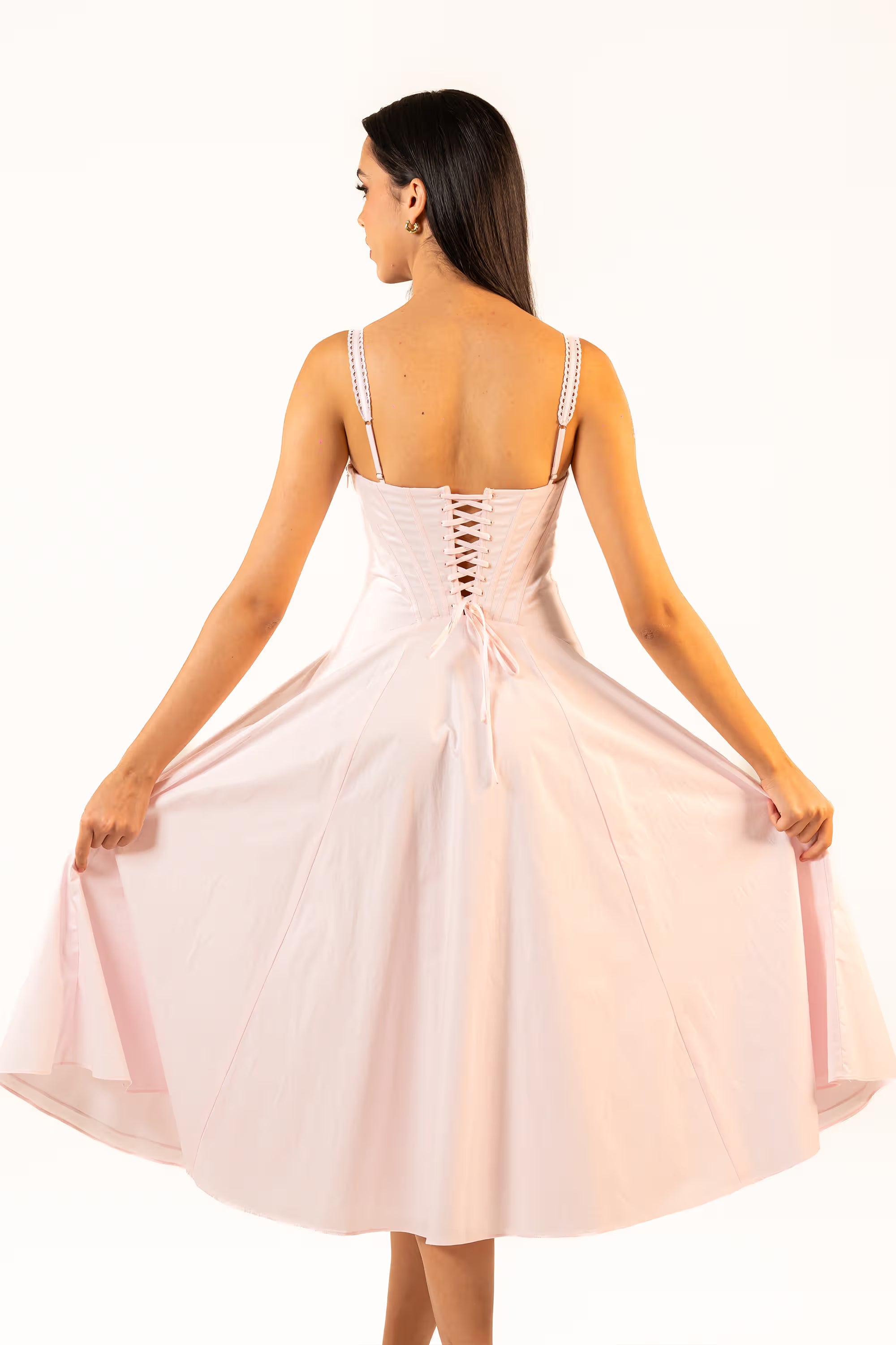 Back view of a soft pink corset midi dress featuring lace-up closure and flared hemline.
