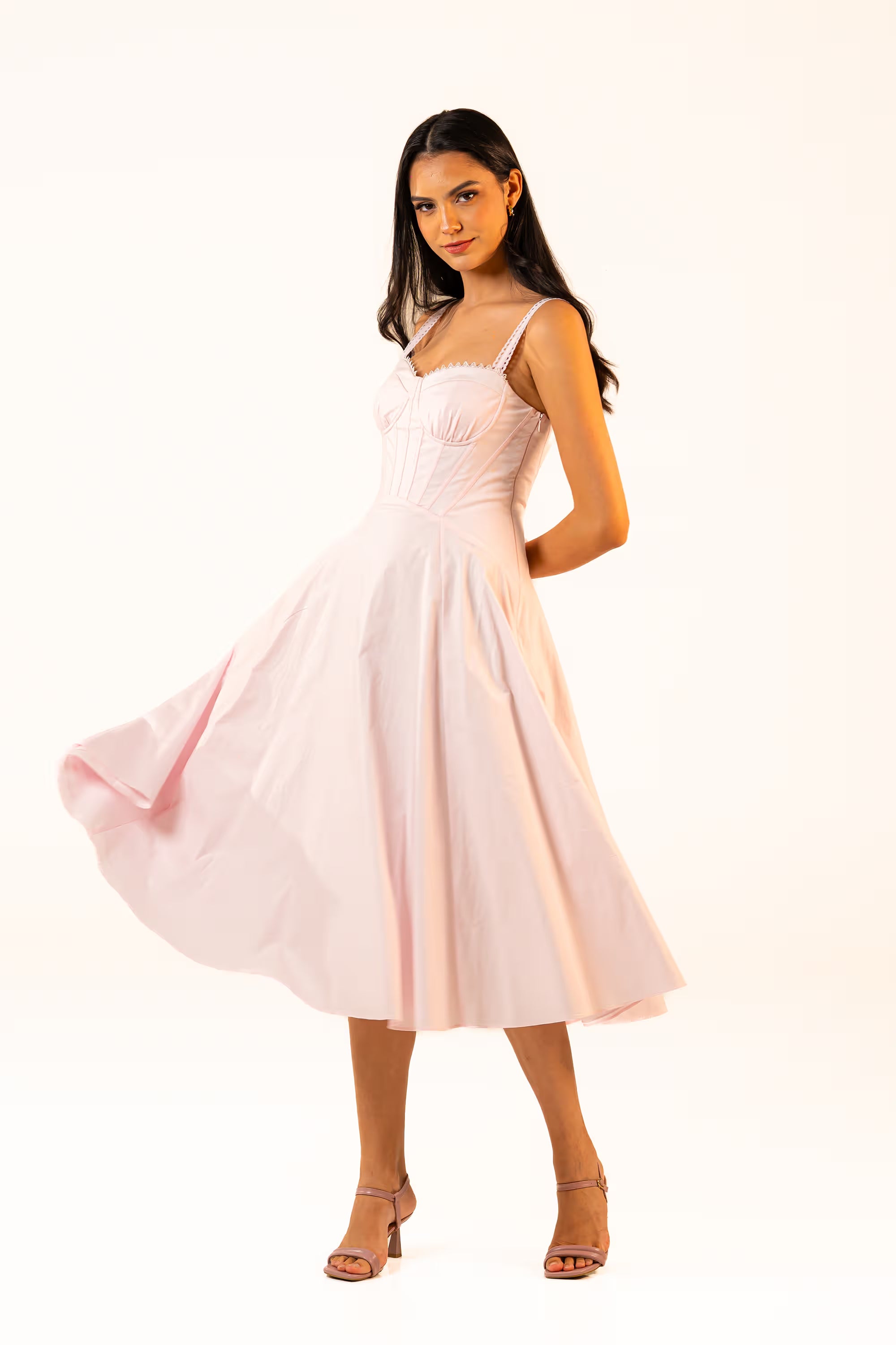 Woman twirling in a soft pink corset midi dress, showcasing the flared silhouette and feminine elegance.