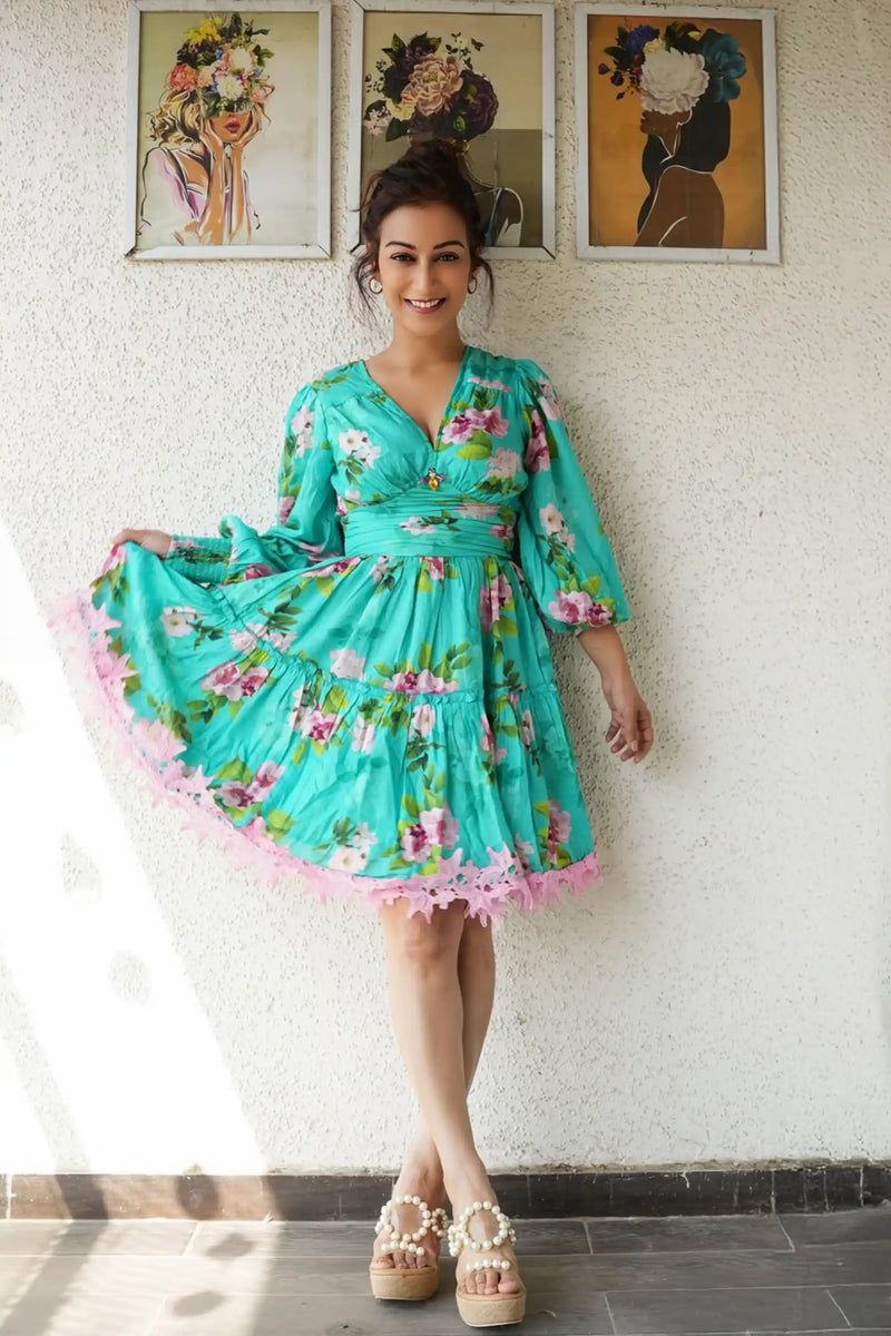 Sunayana Fozdar wearing a turquoise floral dress with a flowing silhouette, posing indoors against a textured wall during a fashion pretty pixie.