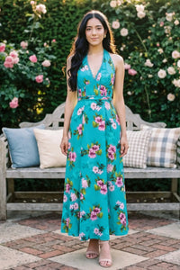 Woman in turquoise floral halter maxi dress with pink and white flowers at garden bench; organic cotton women's occasion wear