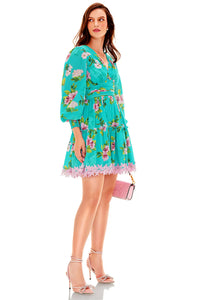 Side view of turquoise floral lace mini dress with long sleeves and pink lace hem