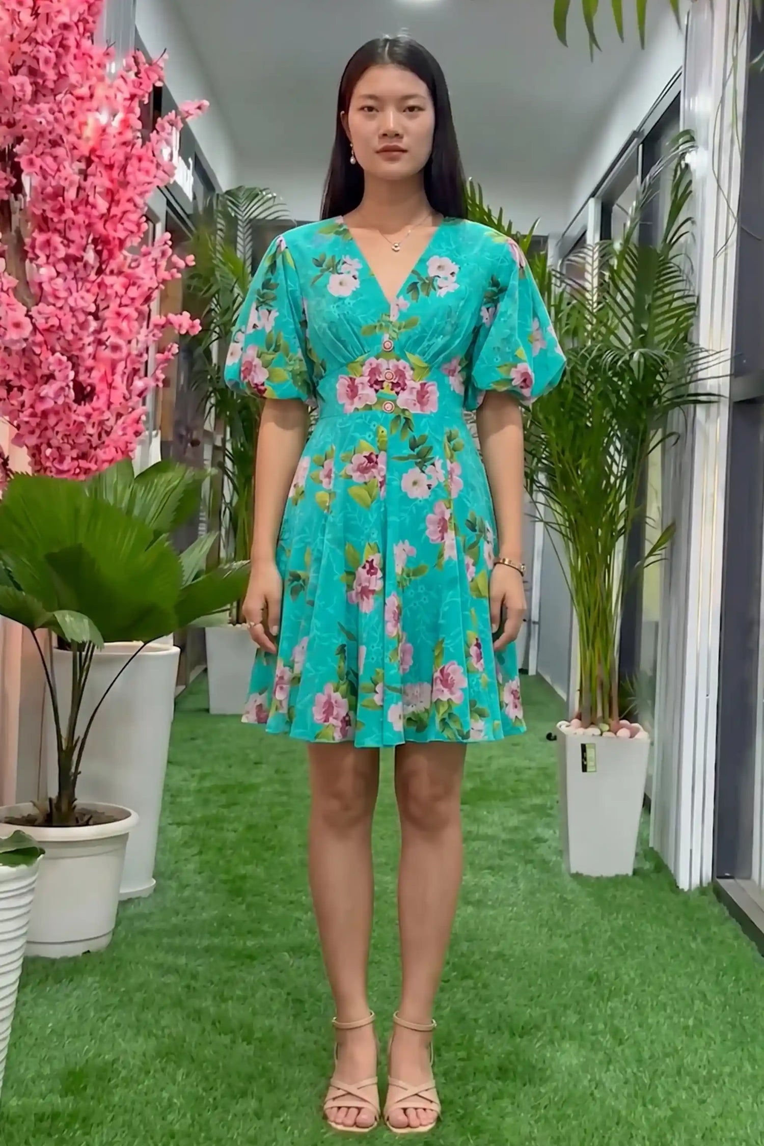 Woman in turquoise floral mini dress with deep V-neck, short puff sleeves and flared skirt