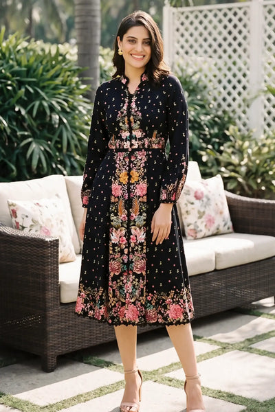 Woman in Twilight Garden black ditsy floral border midi dress with dotted print and mandarin collar smiling on patio lounge with rattan sofa - Pretty Pixie daywear