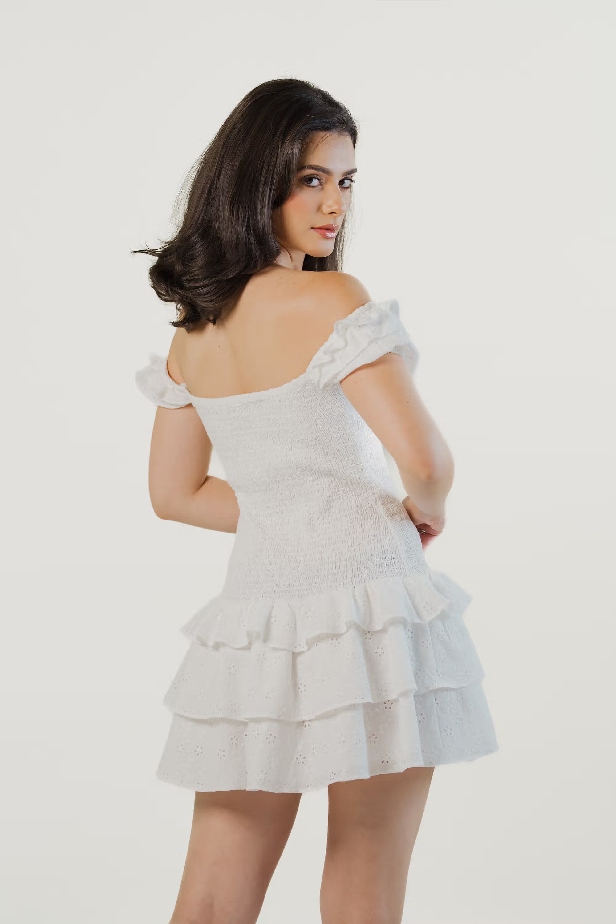 Back view of a white off-shoulder eyelet mini dress with tiered ruffle skirt and smocked bodice.