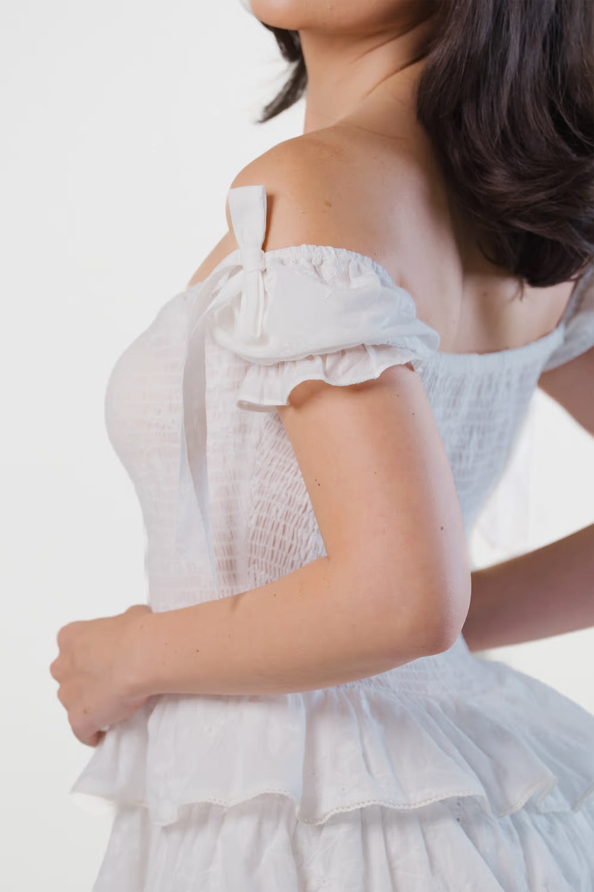 Back view of a woman in a white off-shoulder tiered mini dress with layered ruffles.