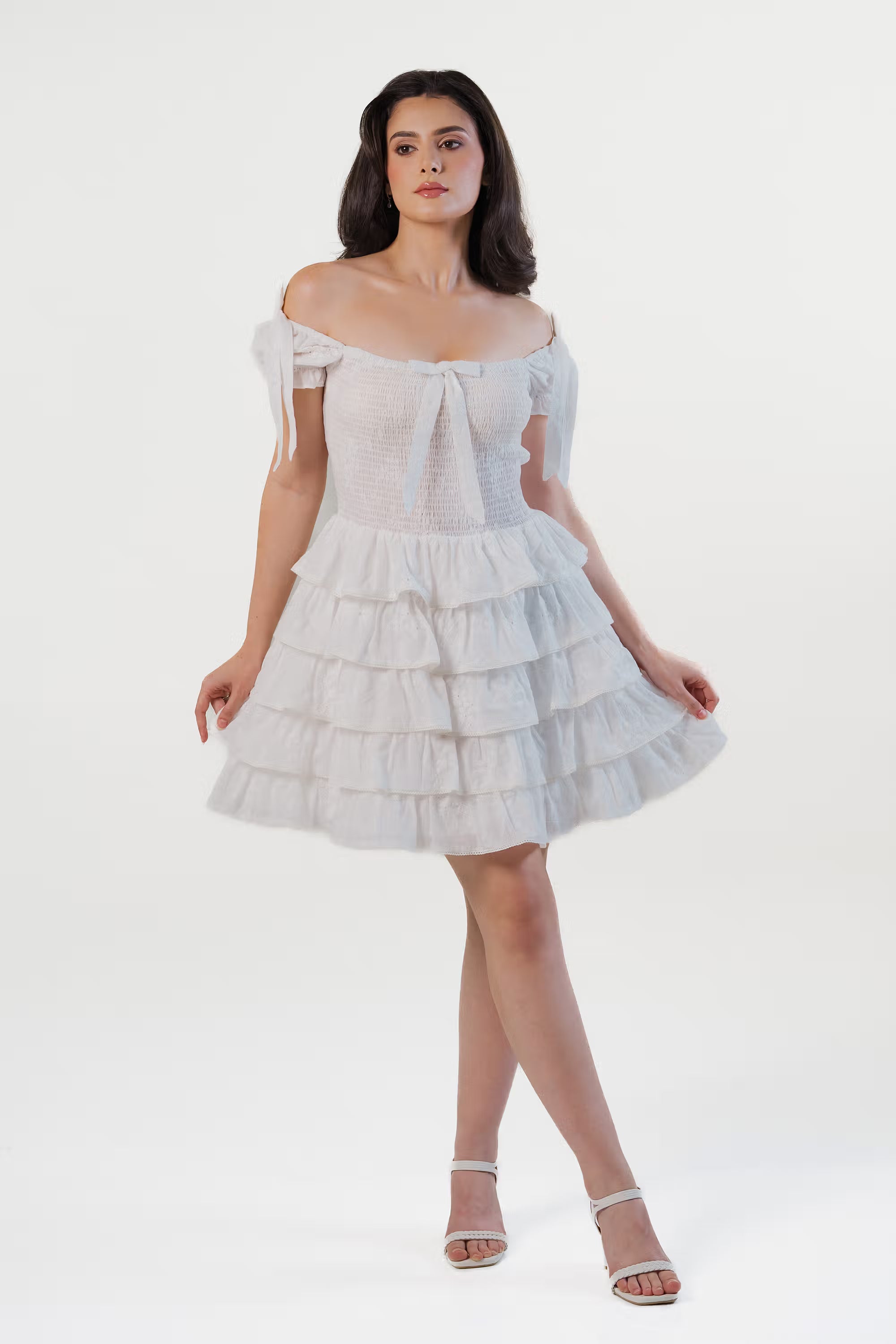 Full-body front view of a woman in a white tiered mini dress with elastic bodice and layered skirt.
