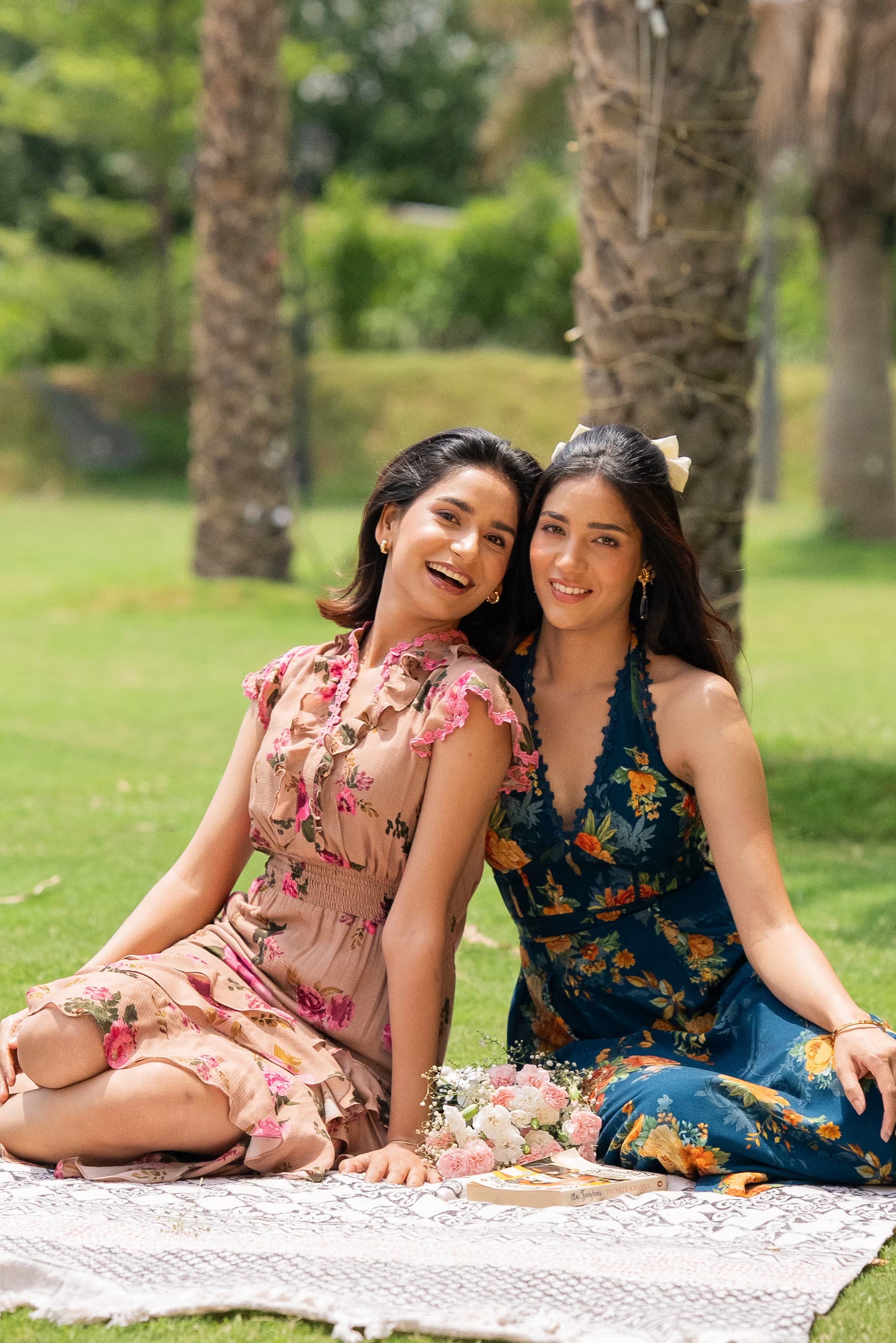 Two women sitting on a blanket in a park with palm trees in the background