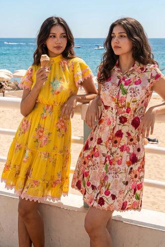 Two women at beach wearing yellow and pink floral organic cotton dresses with lace trim; bright botanical print summer dresses for women